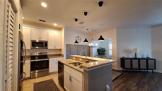 kitchen with pendant lighting, hardwood / wood-style floors, a kitchen island with sink, sink, and appliances with stainless steel finishes