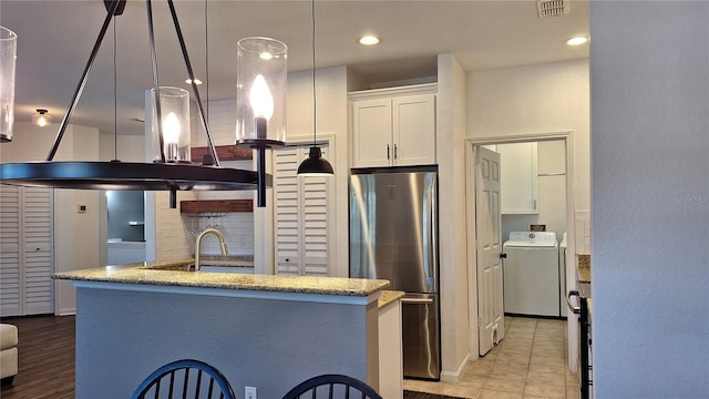 kitchen with stainless steel refrigerator, hanging light fixtures, washer / dryer, white cabinets, and light wood-type flooring