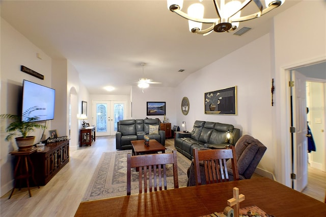 living room with ceiling fan with notable chandelier, light hardwood / wood-style floors, vaulted ceiling, and french doors