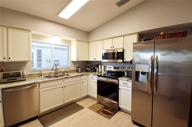 kitchen featuring light stone counters, stainless steel appliances, vaulted ceiling, sink, and light hardwood / wood-style flooring