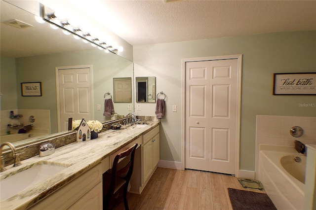 bathroom with hardwood / wood-style floors, vanity, a textured ceiling, and a bathing tub