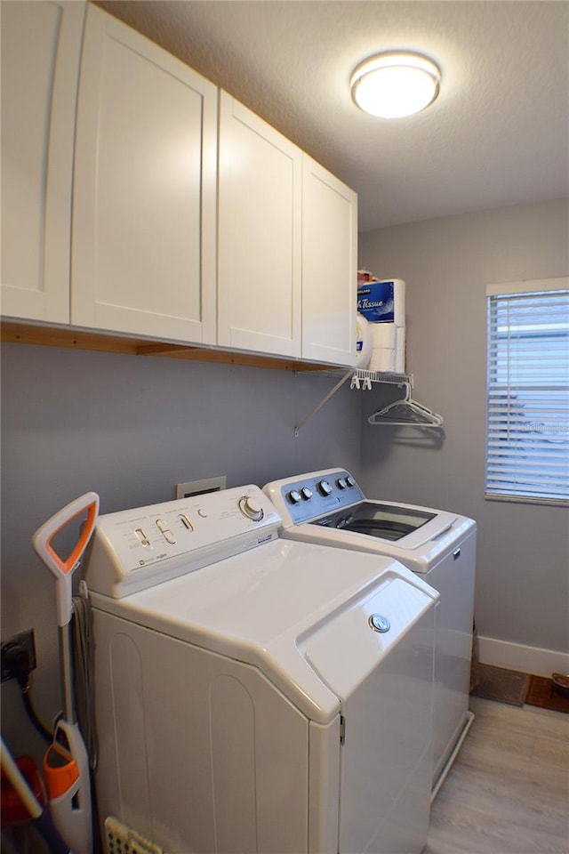 clothes washing area featuring washing machine and dryer, cabinets, and light wood-type flooring