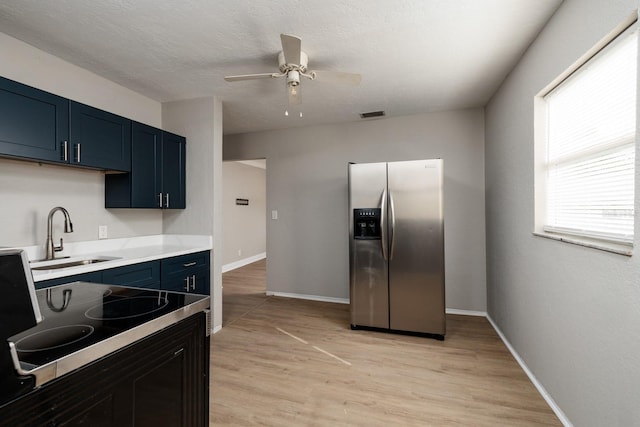 kitchen with sink, stainless steel refrigerator with ice dispenser, blue cabinetry, a textured ceiling, and light hardwood / wood-style flooring