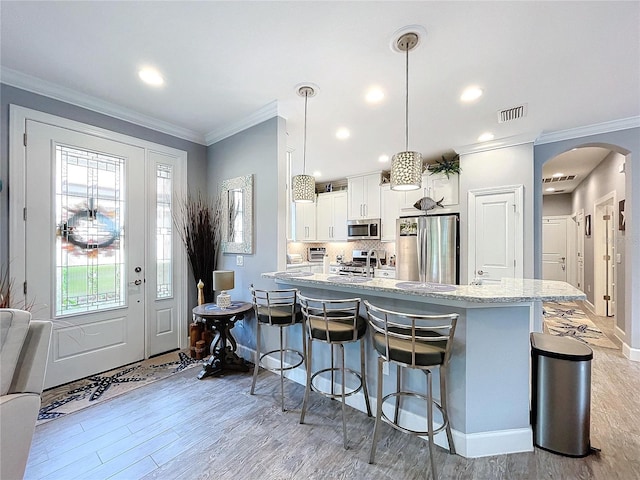 kitchen with tasteful backsplash, decorative light fixtures, light hardwood / wood-style floors, white cabinetry, and stainless steel appliances