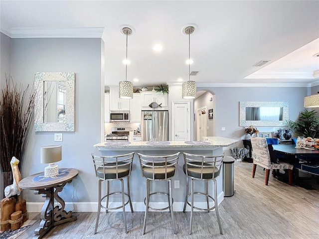 kitchen featuring ornamental molding, stainless steel appliances, pendant lighting, white cabinets, and light hardwood / wood-style floors