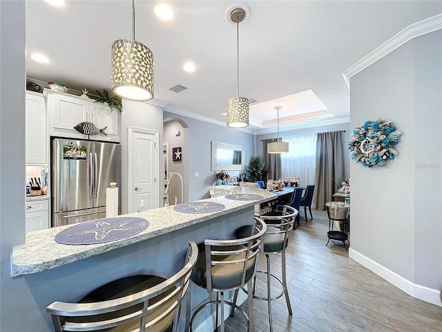 kitchen featuring a kitchen bar, white cabinetry, stainless steel refrigerator, and hanging light fixtures