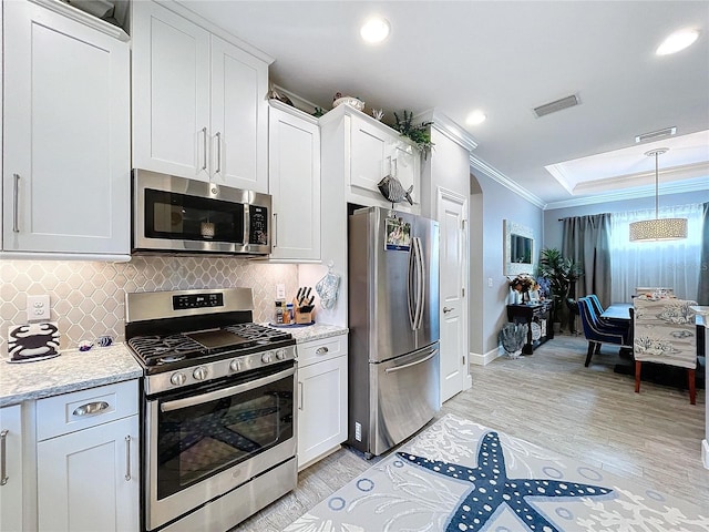 kitchen with white cabinets, crown molding, light hardwood / wood-style flooring, light stone countertops, and appliances with stainless steel finishes