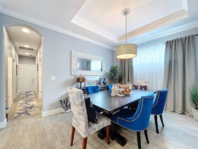 dining room featuring a raised ceiling, crown molding, and light wood-type flooring