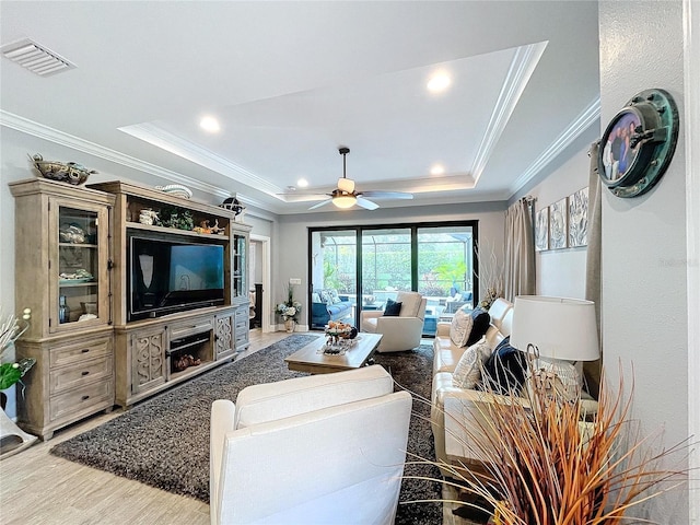 living room featuring a tray ceiling, ceiling fan, crown molding, and light wood-type flooring