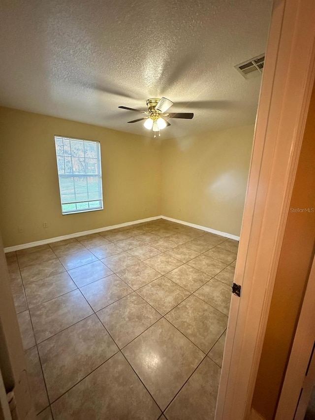 tiled empty room with ceiling fan and a textured ceiling