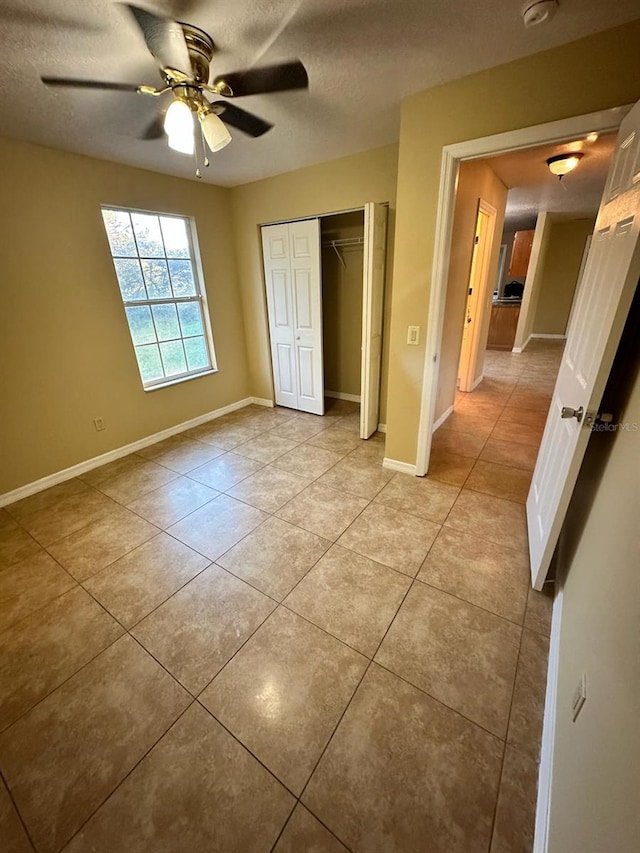 unfurnished bedroom featuring ceiling fan, a closet, light tile patterned floors, and a textured ceiling