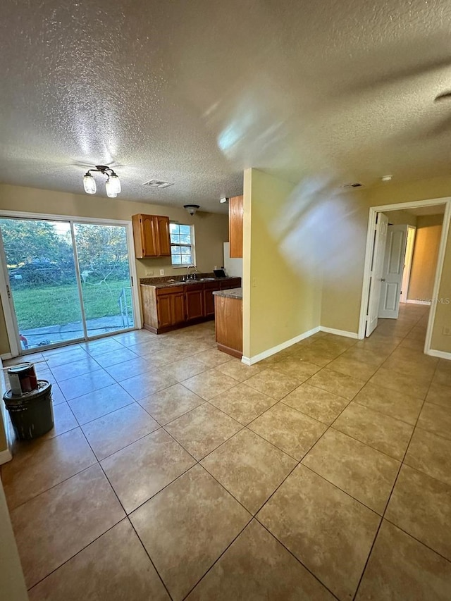 kitchen featuring kitchen peninsula, sink, light tile patterned flooring, and a textured ceiling