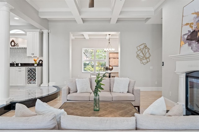 living room featuring beam ceiling, coffered ceiling, a notable chandelier, light wood-type flooring, and ornamental molding