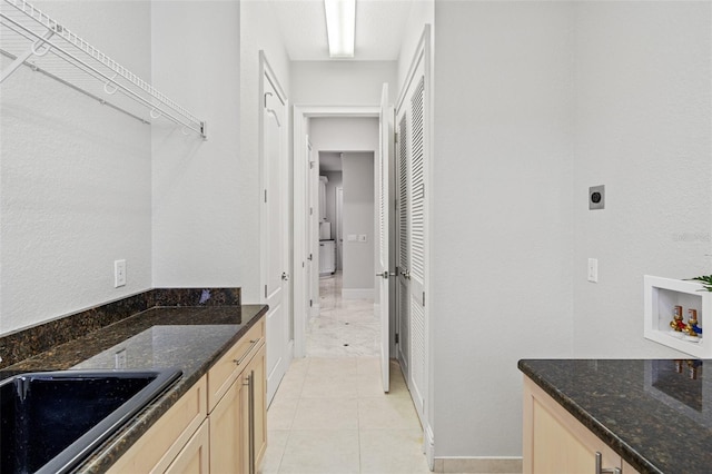 interior space with light brown cabinetry, dark stone countertops, and sink