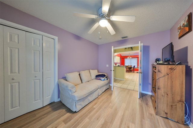 living room featuring wood-type flooring, a textured ceiling, and ceiling fan