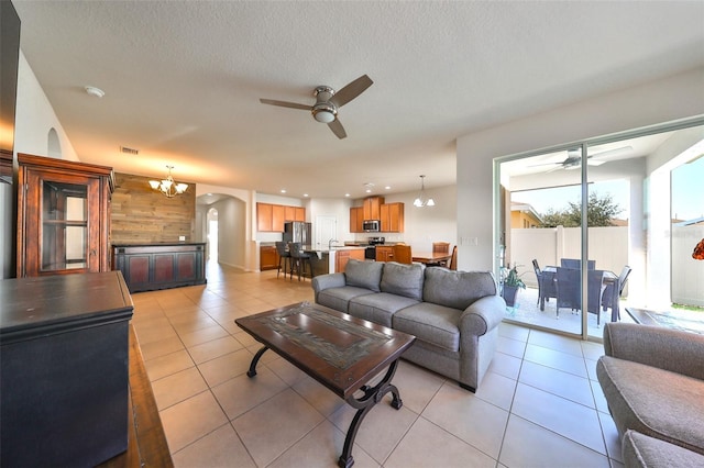 living area with arched walkways, light tile patterned floors, and ceiling fan with notable chandelier