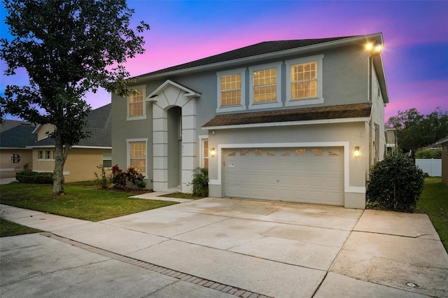 traditional home with stucco siding, a front lawn, driveway, roof with shingles, and a garage