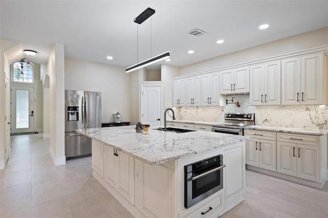 kitchen with appliances with stainless steel finishes, sink, backsplash, and an island with sink