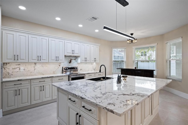 kitchen featuring tasteful backsplash, sink, electric stove, decorative light fixtures, and an island with sink