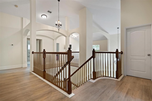 stairway with hardwood / wood-style flooring, a notable chandelier, and high vaulted ceiling