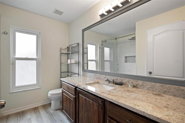 bathroom with visible vents, toilet, wood finished floors, a shower stall, and vanity