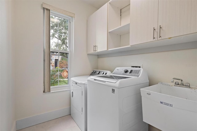 laundry room with baseboards, light tile patterned floors, washer and dryer, cabinet space, and a sink