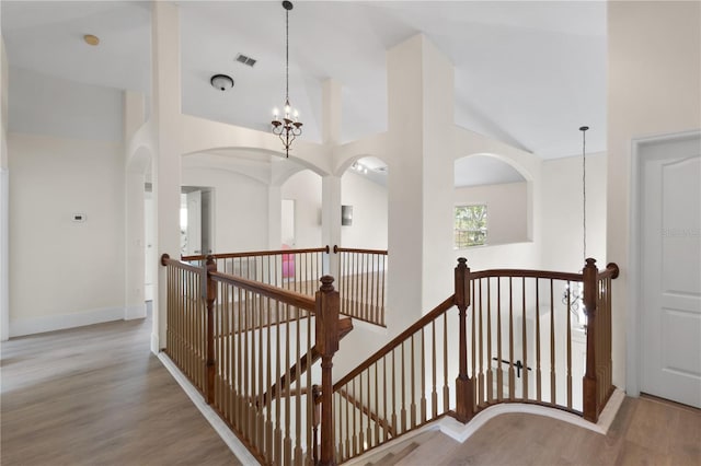 hall featuring wood finished floors, visible vents, baseboards, a towering ceiling, and an upstairs landing