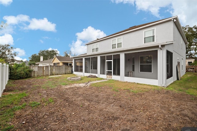 rear view of property featuring an outdoor fire pit, stucco siding, fence private yard, and a sunroom