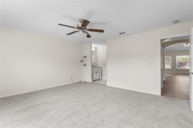 carpeted empty room featuring visible vents, arched walkways, and a ceiling fan