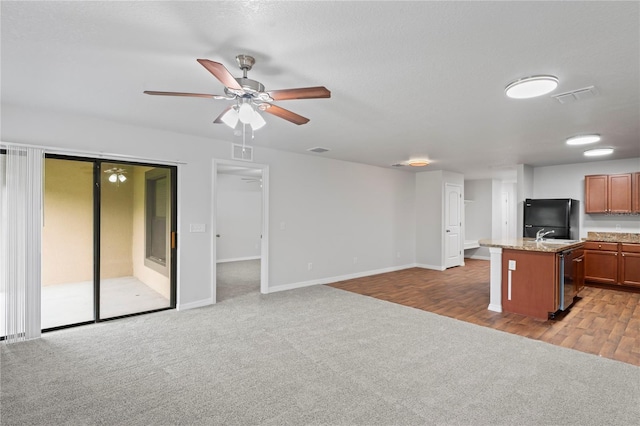 kitchen featuring ceiling fan, light stone countertops, black fridge, light hardwood / wood-style flooring, and a kitchen island with sink