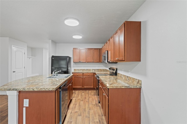 kitchen with a center island with sink, sink, light wood-type flooring, a textured ceiling, and appliances with stainless steel finishes