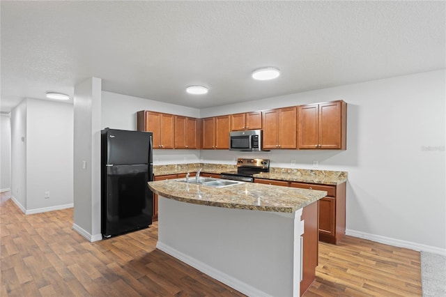 kitchen with light wood-type flooring, light stone counters, stainless steel appliances, a kitchen island with sink, and sink