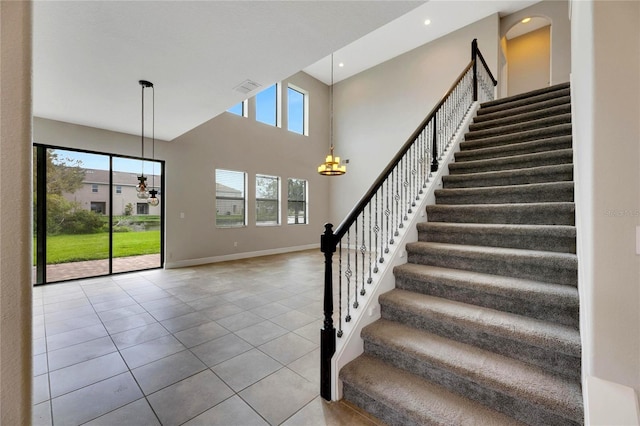 stairway with tile patterned flooring, a high ceiling, a wealth of natural light, and a chandelier