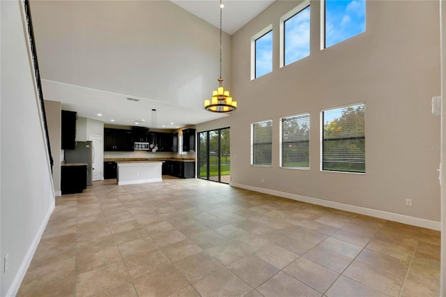 unfurnished living room with a towering ceiling, an inviting chandelier, a wealth of natural light, and light tile patterned flooring