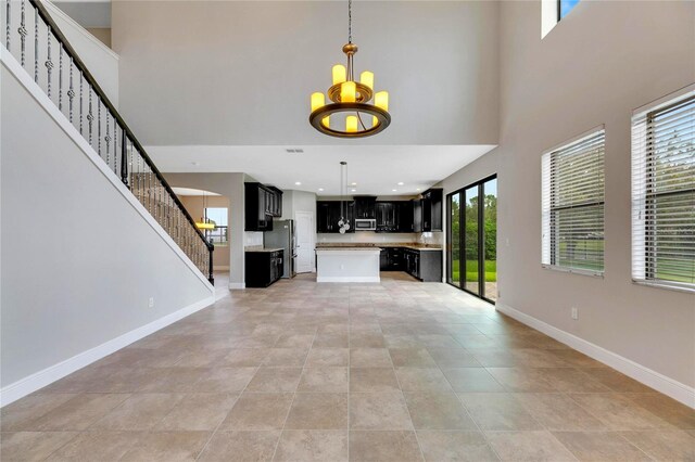 unfurnished living room featuring a towering ceiling, light tile patterned flooring, and a notable chandelier