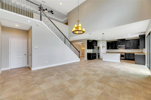 unfurnished living room featuring sink, light tile patterned floors, a high ceiling, and a notable chandelier