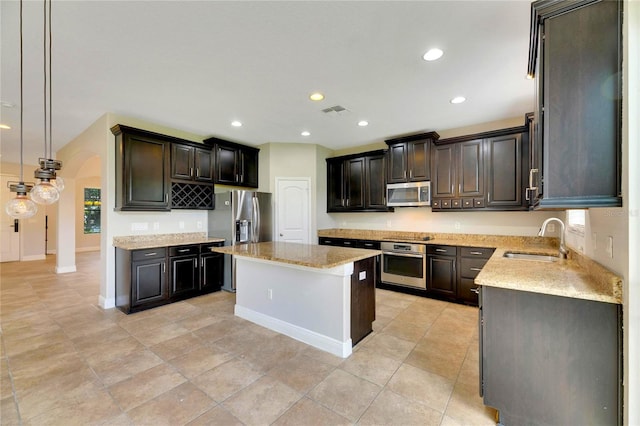 kitchen featuring a center island, hanging light fixtures, sink, light stone countertops, and appliances with stainless steel finishes