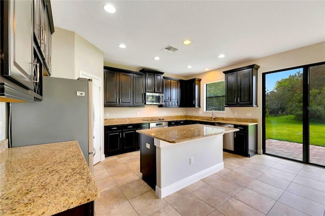 kitchen with light stone countertops, sink, light tile patterned floors, a kitchen island, and appliances with stainless steel finishes