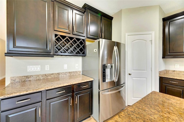 kitchen featuring light stone countertops, stainless steel fridge with ice dispenser, and dark brown cabinetry