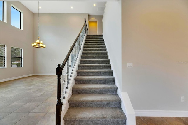 stairway with tile patterned floors, plenty of natural light, a towering ceiling, and an inviting chandelier