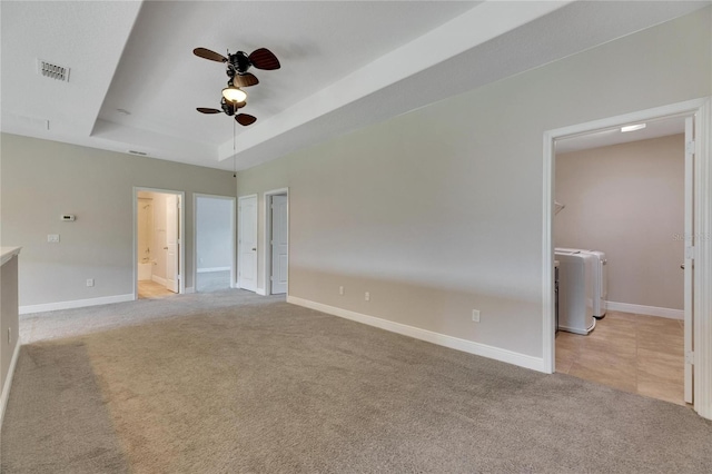 carpeted empty room with a tray ceiling, ceiling fan, and washer / dryer