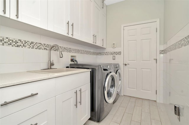 clothes washing area featuring washing machine and clothes dryer, sink, cabinets, and tile walls