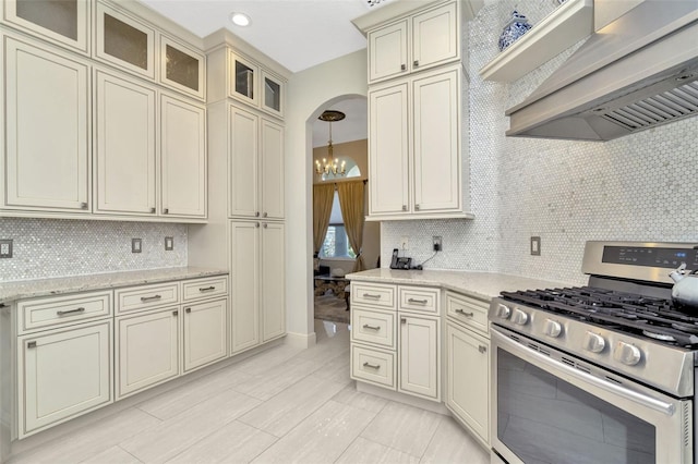 kitchen with cream cabinetry, decorative backsplash, wall chimney range hood, and stainless steel gas range