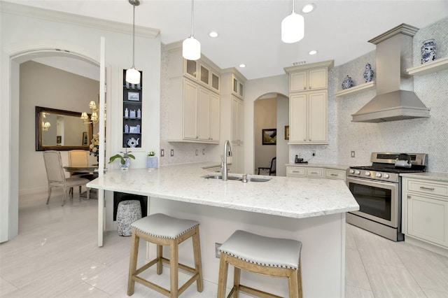 kitchen featuring cream cabinetry, a kitchen breakfast bar, stainless steel stove, and wall chimney range hood