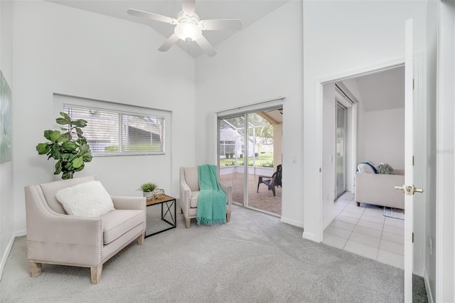 sitting room featuring a towering ceiling, light colored carpet, and ceiling fan