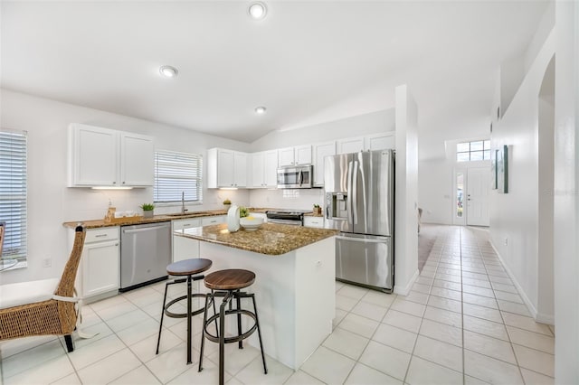 kitchen featuring white cabinetry, appliances with stainless steel finishes, a kitchen breakfast bar, a kitchen island, and dark stone counters