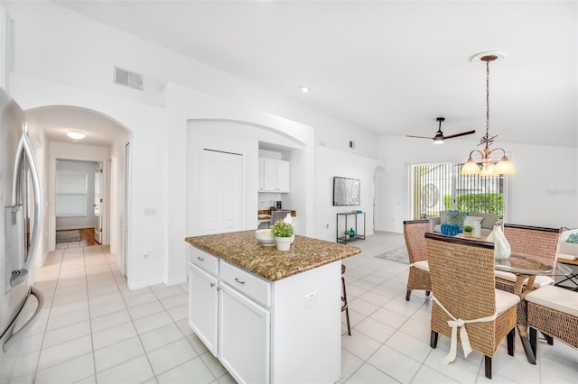 kitchen featuring a kitchen island, dark stone countertops, stainless steel fridge, white cabinets, and hanging light fixtures