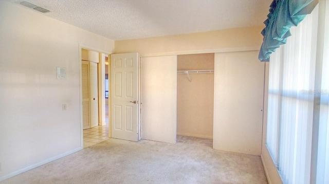 unfurnished bedroom with a closet, light colored carpet, and a textured ceiling