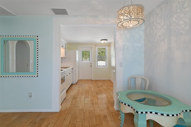 kitchen featuring white cabinets, white range with electric cooktop, hanging light fixtures, a notable chandelier, and light hardwood / wood-style floors