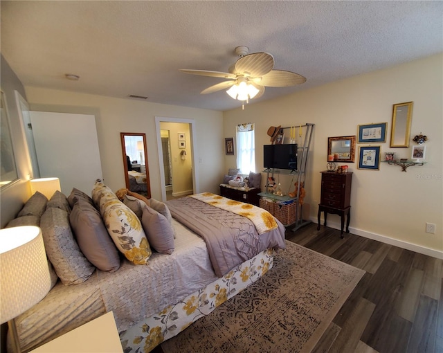 bedroom with a textured ceiling, ceiling fan, dark wood-type flooring, and connected bathroom